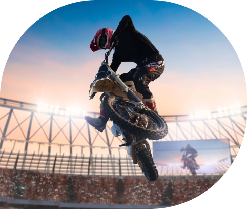 Un cascadeur à moto en plein vol dans un grand stade, éclairé par de puissants projecteurs. Le ciel présente un dégradé de bleu et d'orange, ajoutant à l'atmosphère palpitante.
